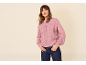 Vrouw in een roze vest met knopen en donkerblauwe jeans, handen in zakken.