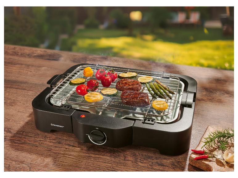 Elektrische grill met groenten en vlees op een houten tafel buiten.