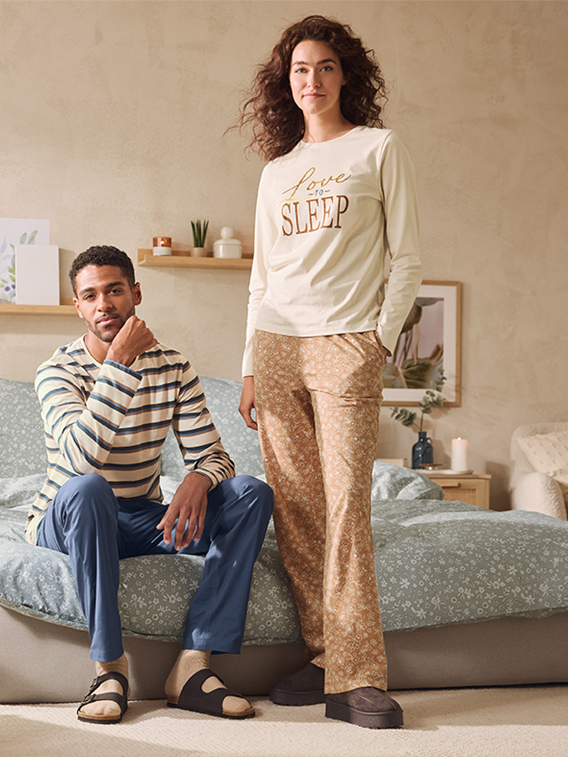 Een stel draagt bijpassende pyjama's, hij in strepen en blauwe broek, zij in een 'Love to Sleep' top en een broek met patroon.