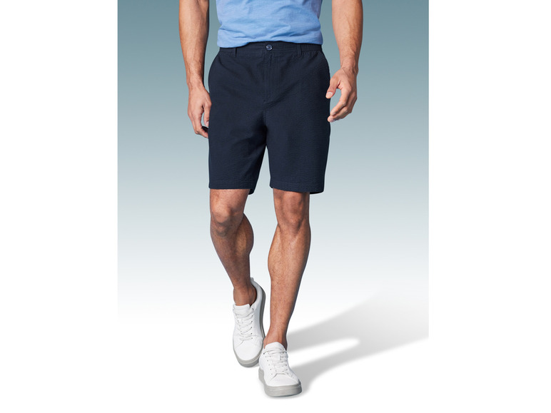 Man draagt donkerblauwe shorts en witte sneakers.