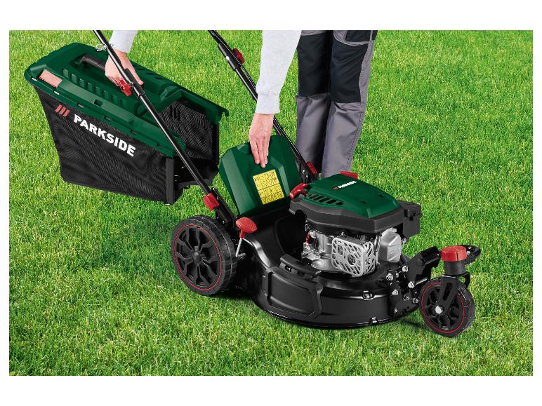Persoon die een benzine grasmaaier met grasopvangbak klaarmaakt voor gebruik op een groen gazon.