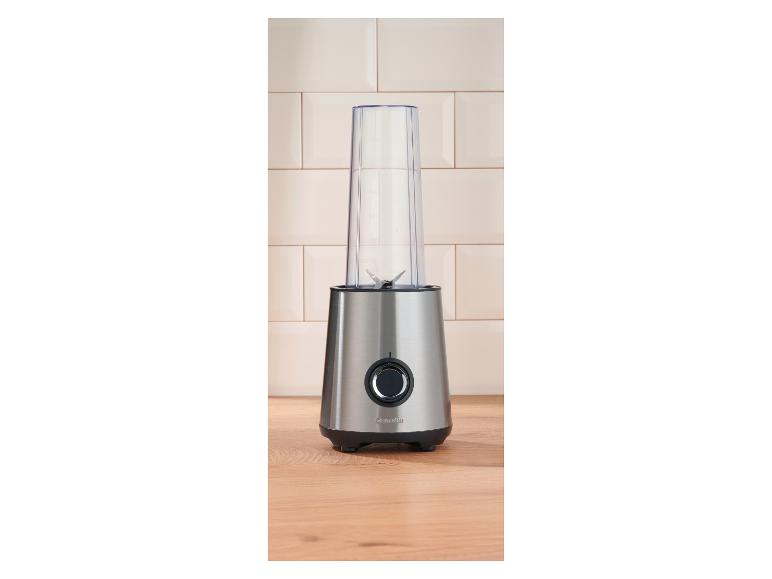 Roestvrijstalen blender met transparante beker op een houten aanrecht.