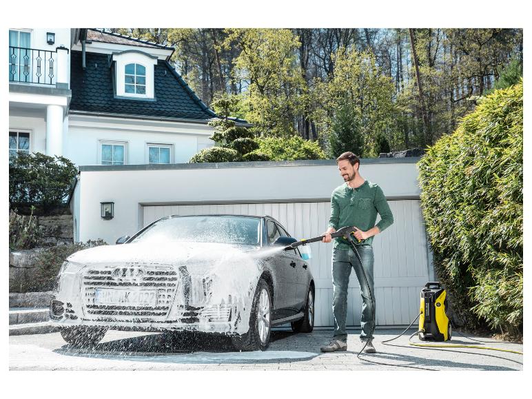 Man wast auto met hogedrukreiniger voor een huis.