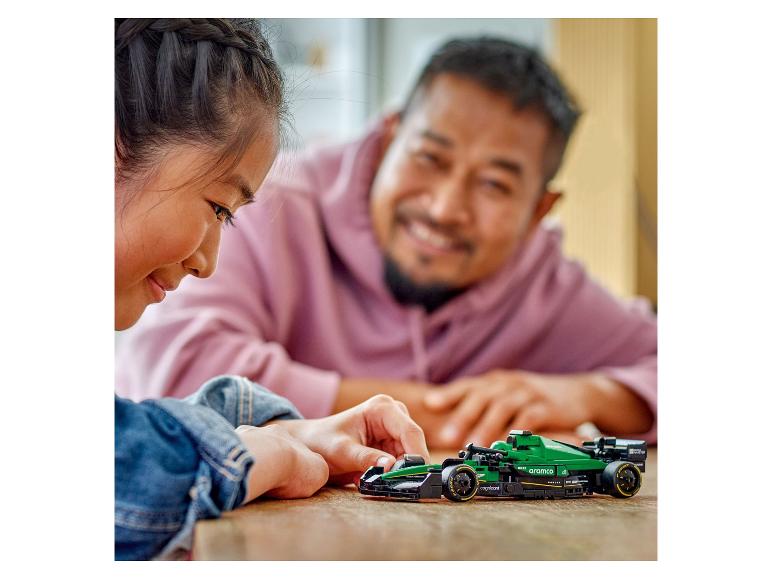 Een meisje en een man spelen met een groene Aston Martin Aramco raceauto.