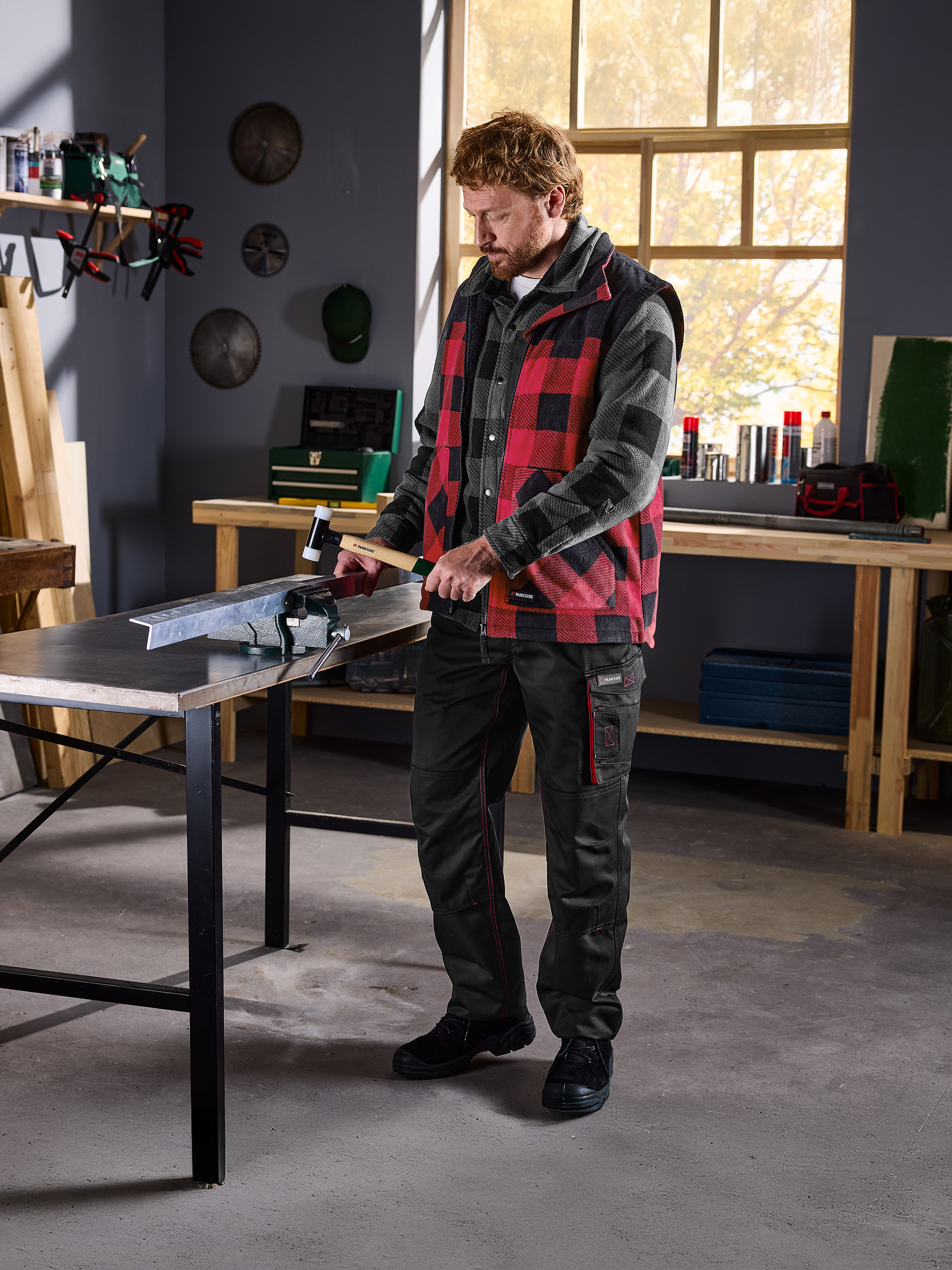 Man in geruit overhemd en Parkside-vest bewerkt metaal in een bankschroef in een werkplaats.