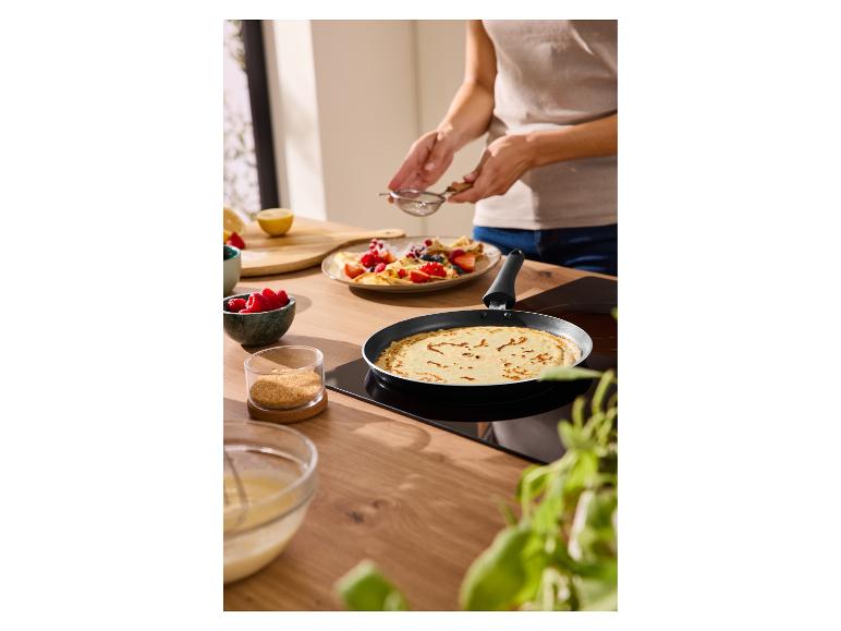 Persoon bereidt pannenkoeken met bosvruchten en suiker in een pan in de keuken.