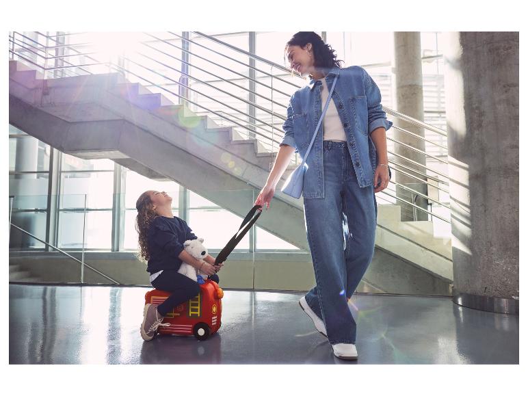 Een meisje rijdt op een rode koffer in de vorm van een brandweerauto.