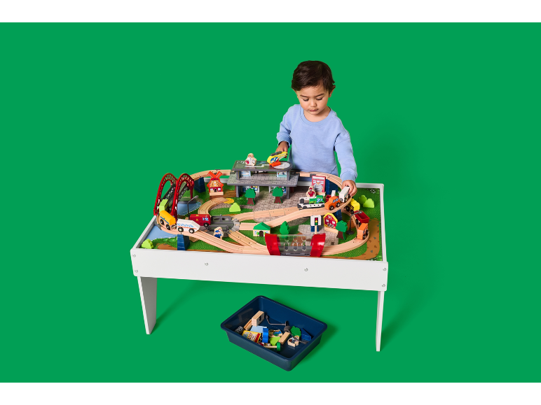 Kind speelt met een houten speeltafel met treinbaan en accessoires.