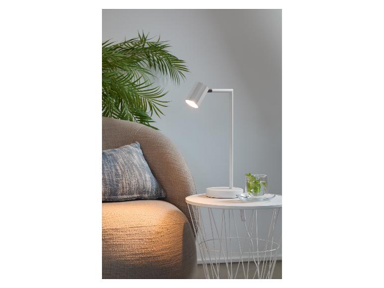 Moderne witte tafellamp naast een comfortabele fauteuil.