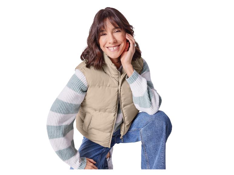Lachende vrouw in een beige vest en gestreepte trui.