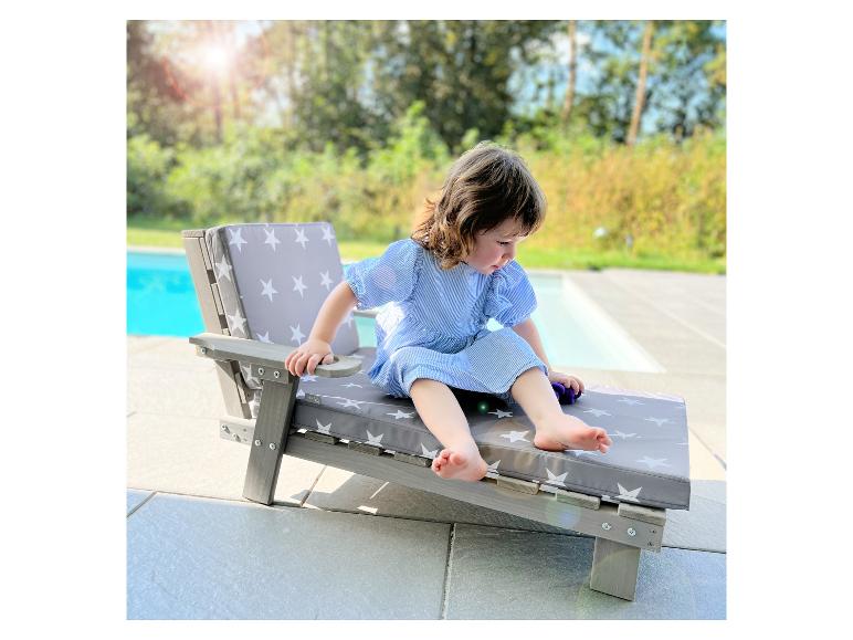 Peuter op een houten ligstoel met grijze kussens met witte sterren naast een zwembad.