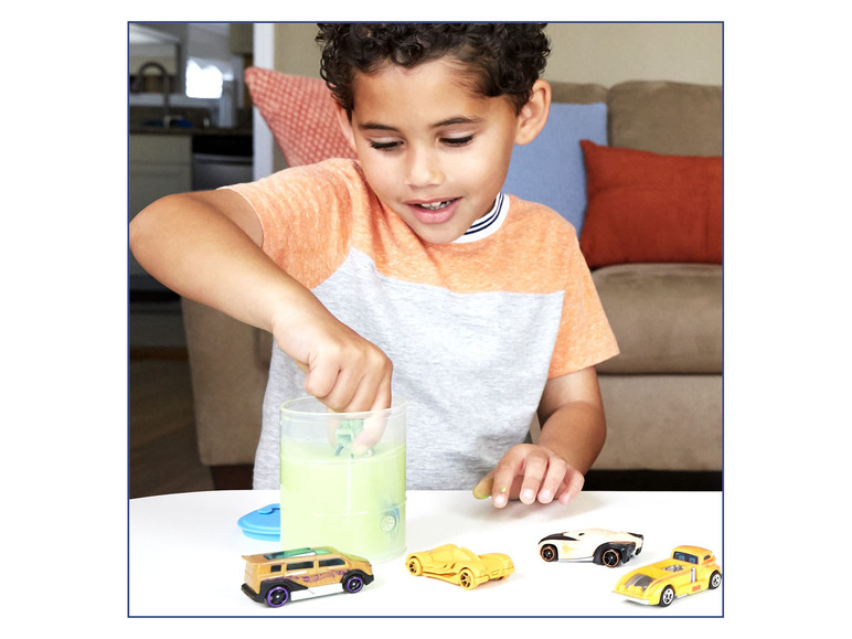 Een jongen speelt met Hot Wheels auto's en een slijmcontainer.
