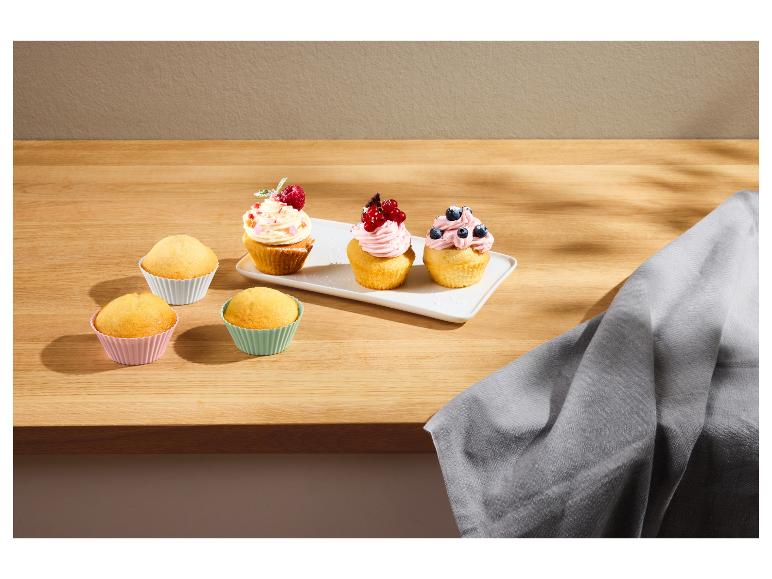 Cupcakes met glazuur en fruit, en gewone cupcakes in kleurrijke vormen op een houten tafel.