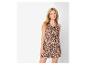 Vrouw in bruine en beige jumpsuit met print met gouden oorbellen en armband