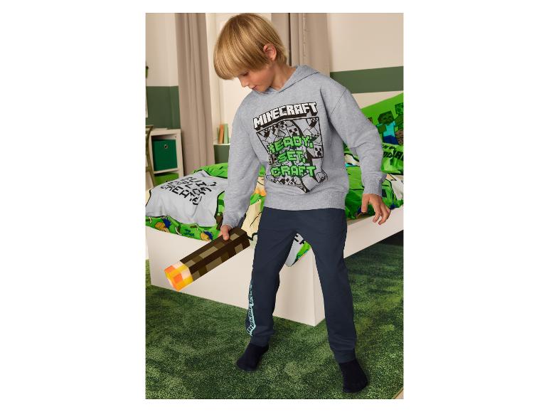 Jongen in Minecraft hoodie en donkerblauwe broek, met een Minecraft fakkel.