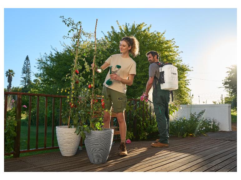 Jonge vrouw begiet tomaten in pot, man besproeit planten op houten terras.