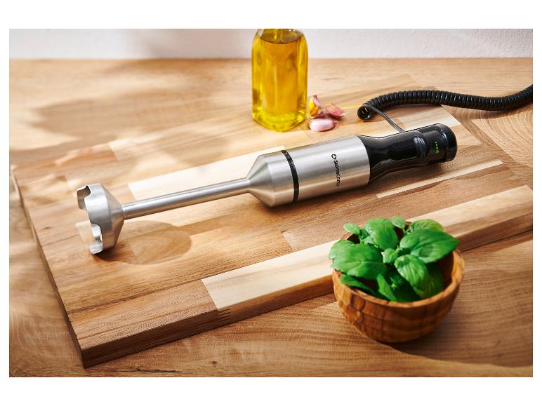 Staafmixer, oliefles, knoflook en basilicum op een houten plank.