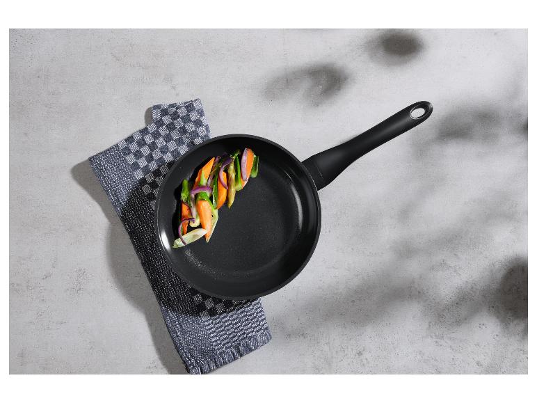 Koekenpan met gesneden groenten op een geruite theedoek op een cementen ondergrond.