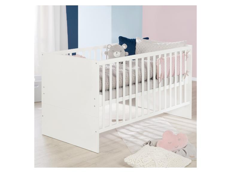 Wit babybedje met grijs beddengoed en decoratieve kussens, in een kamer met tweekleurige muren.