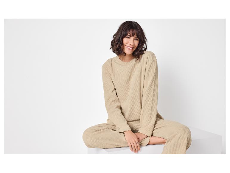 Vrouw in beige geribbelde top en broek zittend, glimlachend.