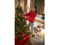 Vrouw versiert kerstboom met lichtjes en ornamenten, cadeaus en decoraties op de poef.