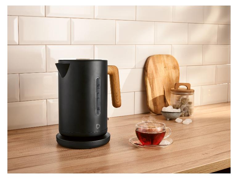 Zwarte waterkoker met houten handvat op een aanrecht met een kopje thee.
