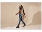 Vrouw in een lange beige bodywarmer, bruine top, jeans en zwarte laarzen loopt.
