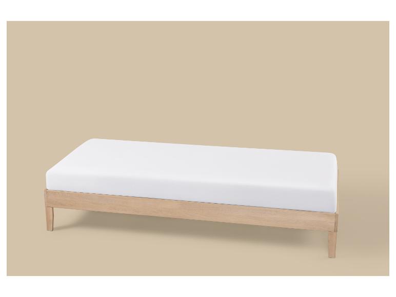 Licht houten bedframe met wit matras op een beige achtergrond