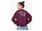 Meisje in bordeauxrode sweatshirt met 'CROISSANT & COFFEE CLUB' op de rug, handen in jeanszakken.