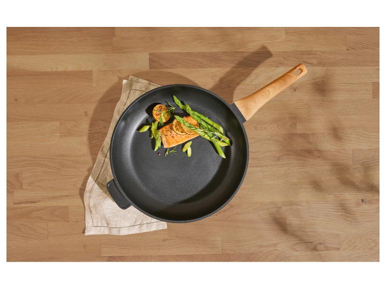 Koekenpan met zalm, asperges en citroen op een houten tafel.