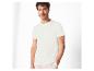 Man in wit T-shirt en beige broek, poserend met hand in zak.