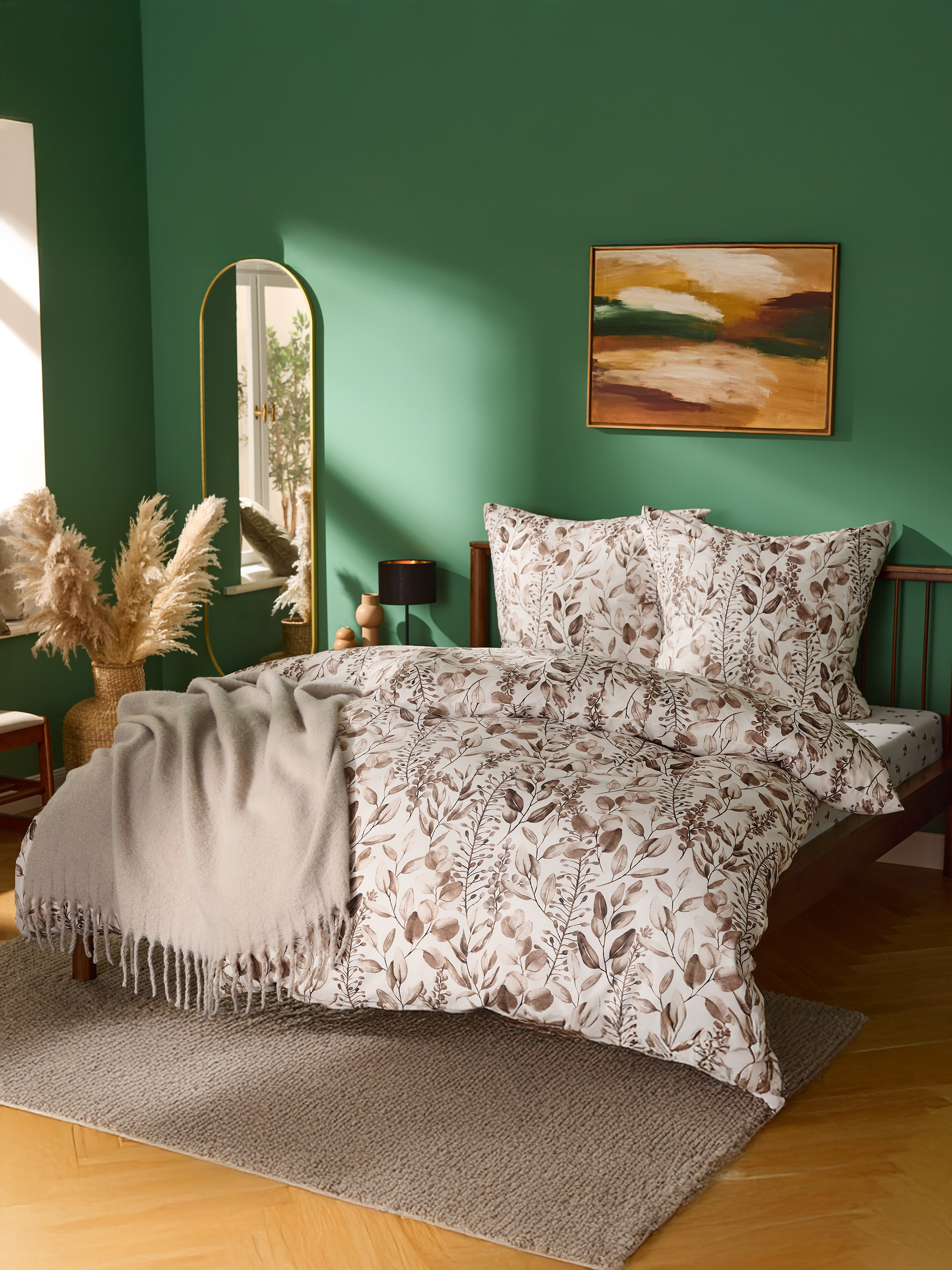 Slaapkamer met groene muren, bed met bladmotief beddengoed en beige deken.