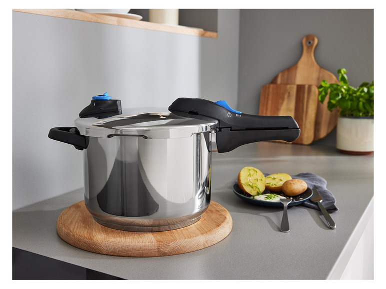 Een zilveren snelkookpan op een houten onderzetter in de keuken.