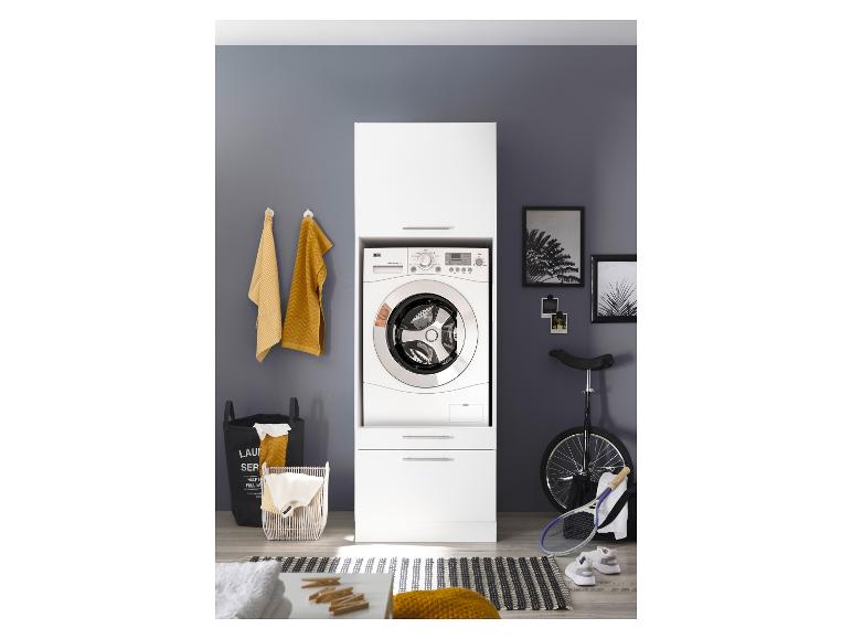 Wasmachine in een witte kast, met wasmanden en sportuitrusting ernaast.