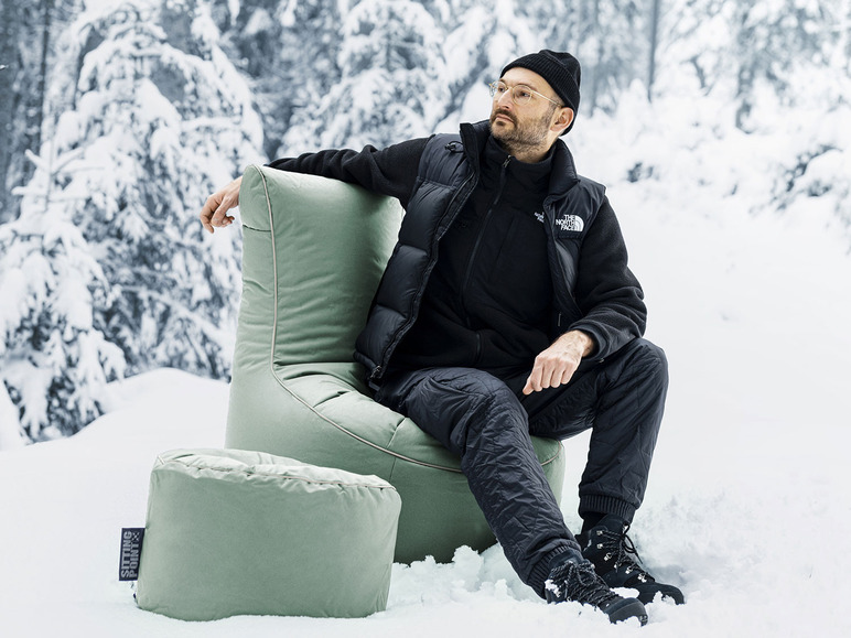 Een man zit in een groene Sitting Point stoel in de sneeuw.
