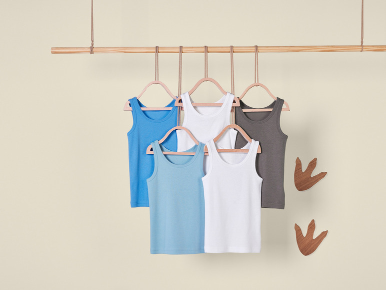 Vier tanktops voor kinderen, in blauw, wit en grijs, met dinosaurusvoetafdrukken op de achtergrond.