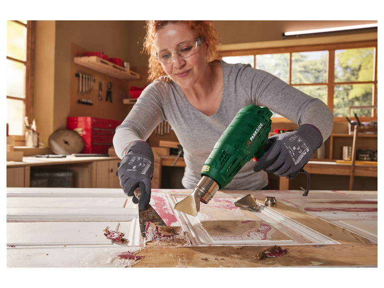 Een vrouw gebruikt een Parkside heteluchtpistool om verf van een deur te verwijderen.