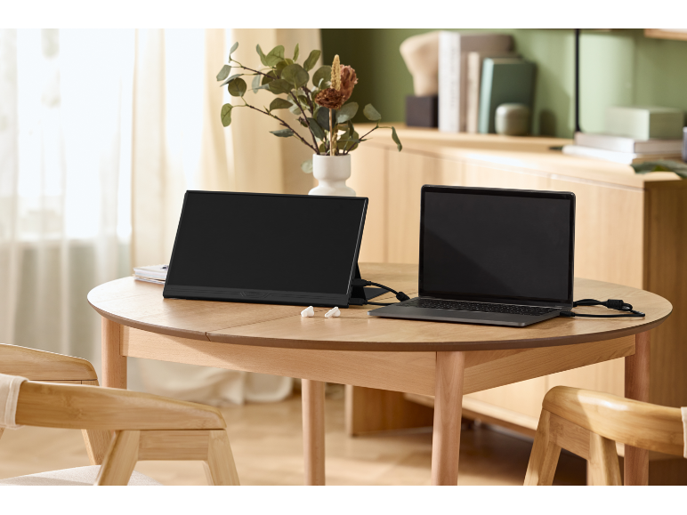 Een draagbare monitor en een laptop aangesloten op een houten tafel in een lichte kamer.