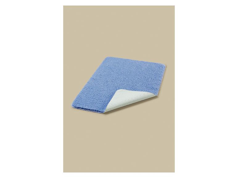 Een rechthoekige blauwe badmat met een witte antislip achterkant, gedeeltelijk opgevouwen.