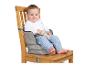 Lachende baby zit in een grijze stoffen zitverhoger op een houten stoel.