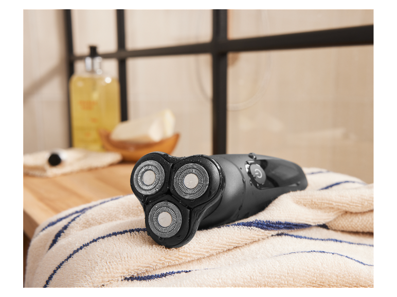 Een nat elektrisch scheerapparaat ligt op een handdoek in een badkamer.