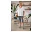Vrouw in wit T-shirt en grijze legging met handtas staat in gezellige kamer.