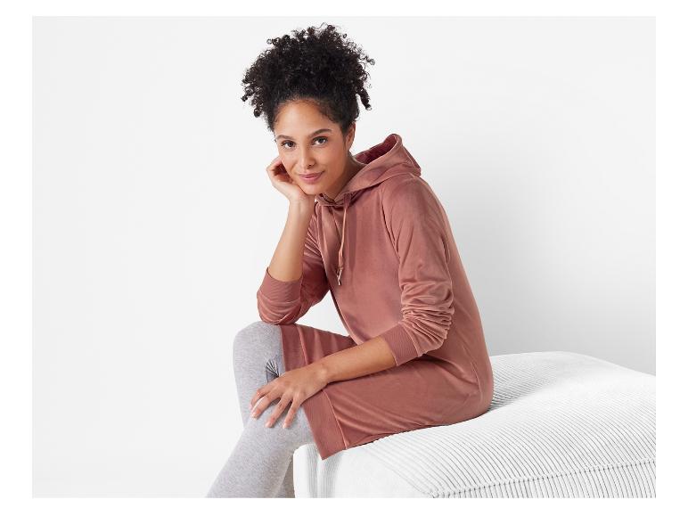 Een vrouw draagt een roze hoodie-jurk met grijze leggings.