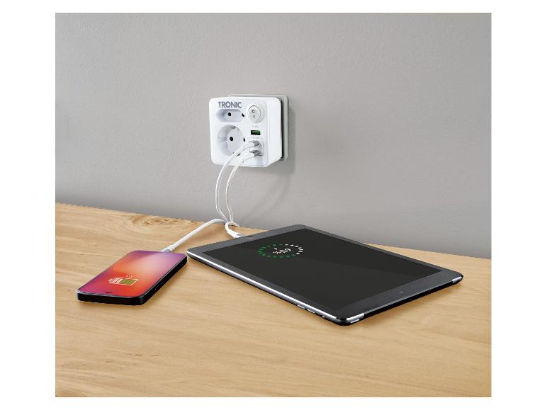 Witte wandcontactdoosadapter met twee USB-poorten die een smartphone en tablet opladen op een houten oppervlak.