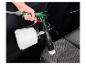 Hand houdt een autoreinigingspistool met borstelopzetstuk vast, reinigt een autostoel.