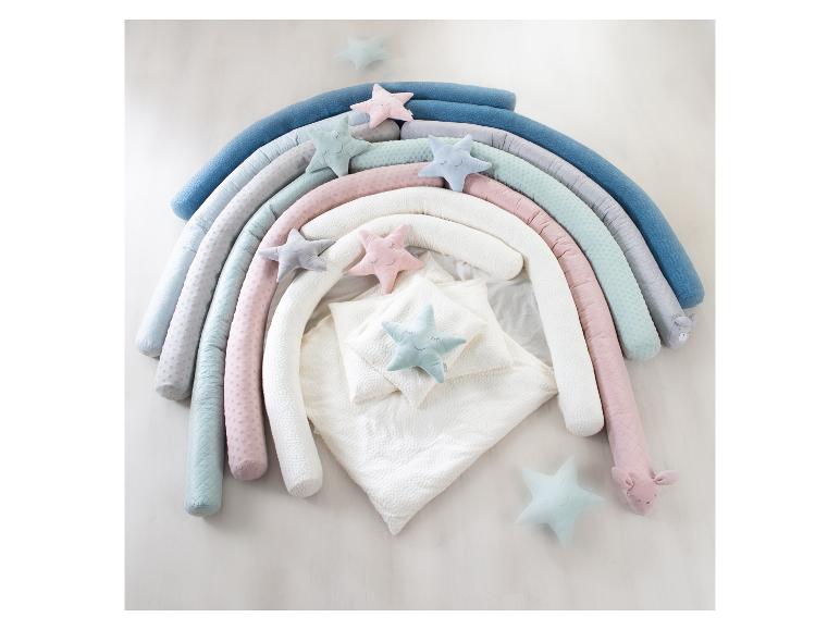 Regenboogvormig babynestje met sterrenkussens en wit beddengoed.