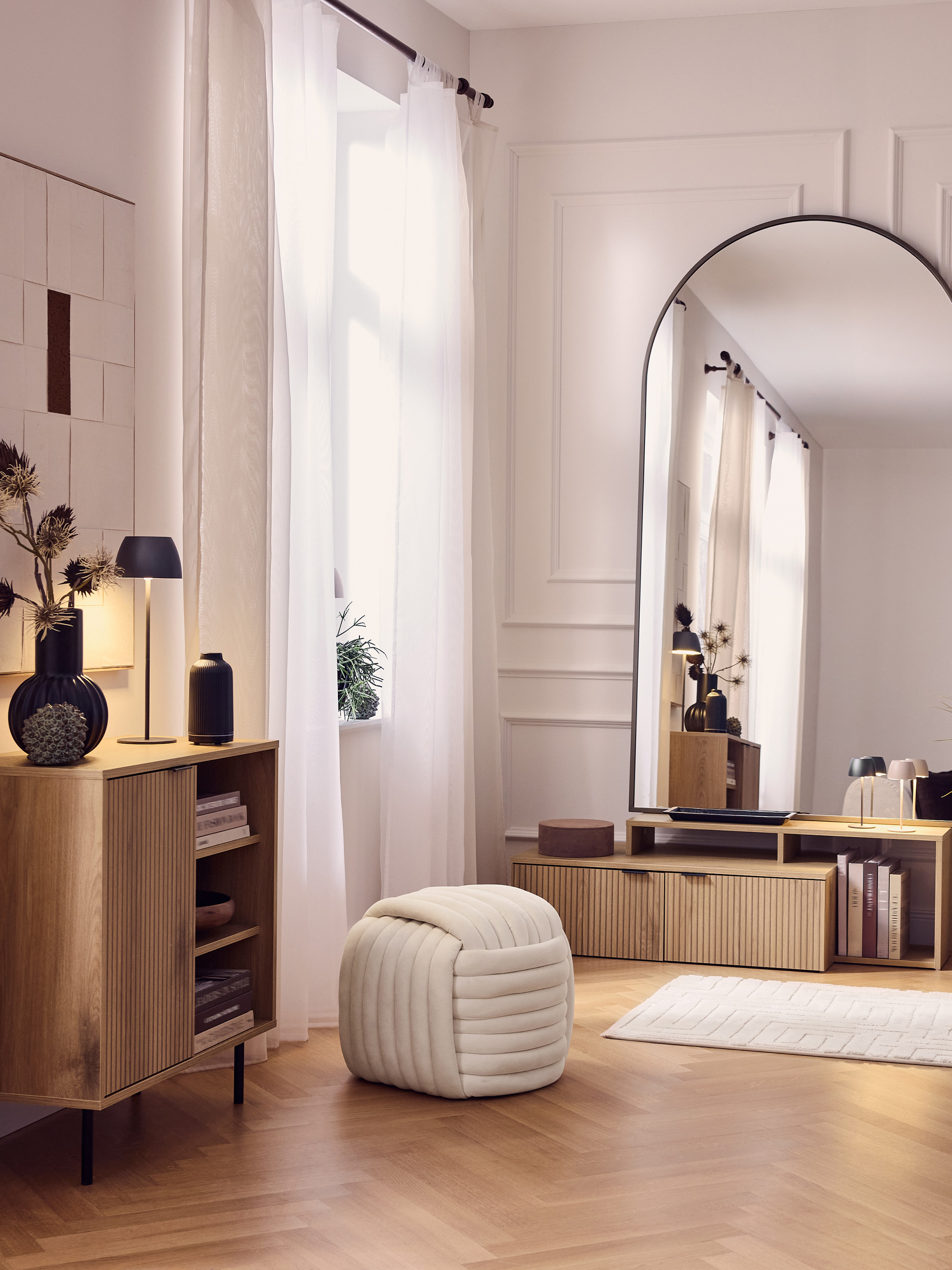 Moderne woonkamer met houten kasten, grote spiegel, poef en witte gordijnen.