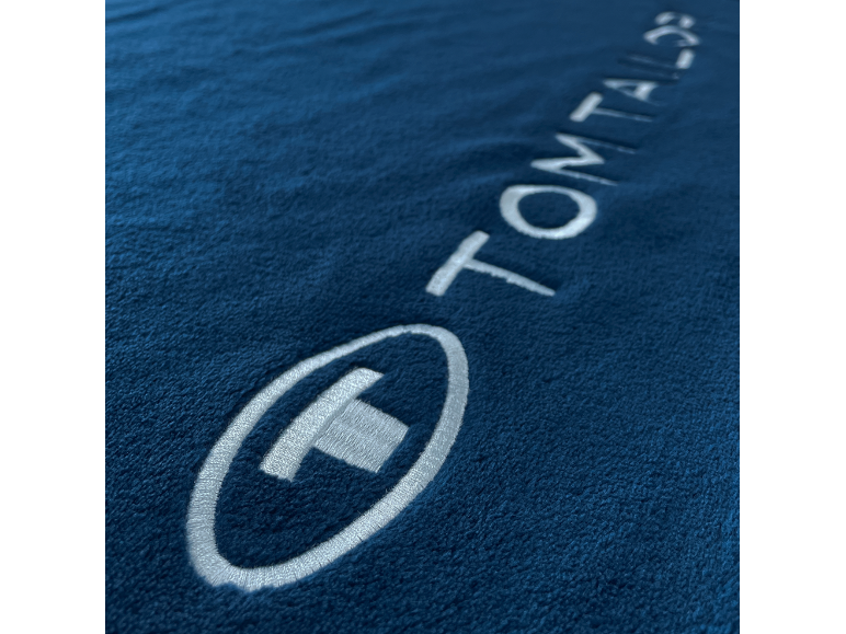 Donkerblauwe stof met een wit geborduurd logo en het woord 'TOM TAILOR'.