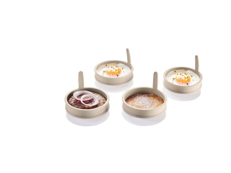 Vier siliconen bakvormen met gebakken eieren, een hamburger en een pannenkoek.