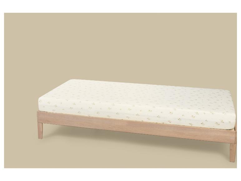 Licht houten eenpersoonsbed met een matras met bloemenpatroon op een beige achtergrond.